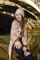 Lächelnde Frau sitzt nachts auf einem Geländer - JRVF02300
