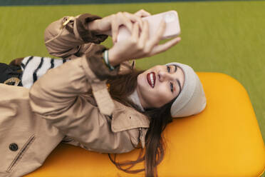 Junge Frau, die ein Smartphone benutzt und auf einer gelben Couch liegt - JRVF02304