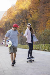 Mann, der die Hand einer Frau hält, die auf dem Gehweg Skateboard fährt - OMIF00230