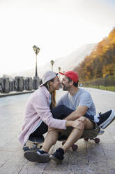 Romantic couple rubbing noses sitting on skateboard at footpath - OMIF00231