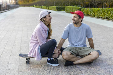 Paar, das auf einem Skateboard sitzend auf dem Gehweg miteinander spricht - OMIF00234