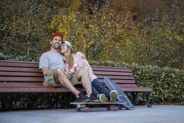 Paar mit Skateboards umarmt einander sitzen auf Bank von Pflanzen - OMIF00238