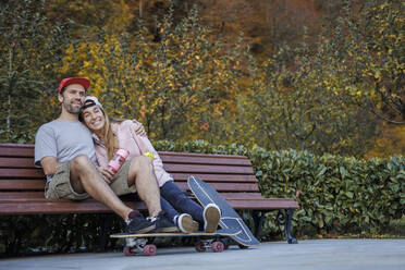 Mann mit Arm um Freundin sitzt zusammen auf Bank bei Pflanzen - OMIF00239
