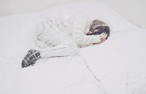 In Plastik gefangene Frau auf Bettdecke liegend an einem engen Ort - SVCF00082