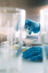 Junge Wissenschaftlerin gießt Flüssigkeit in Glasgefäße auf dem Tisch - ASGF01866