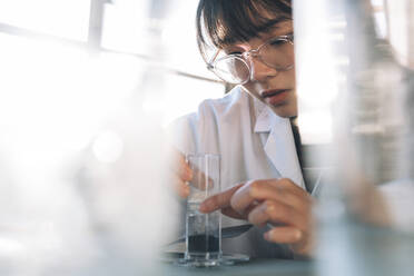 Junge Wissenschaftlerin bei der Untersuchung einer flüssigen Lösung in einem Glasgefäß - ASGF01878
