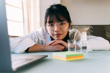Young chemist wearing eyeglasses leaning on table in laboratory - ASGF01879
