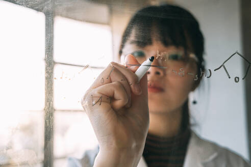 Junge Wissenschaftlerin schreibt auf transparentem Glas im Labor - ASGF01887
