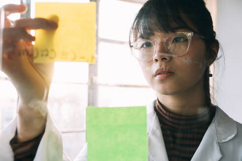 Junge Wissenschaftlerin klebt Haftnotiz auf transparentes Glas - ASGF01889