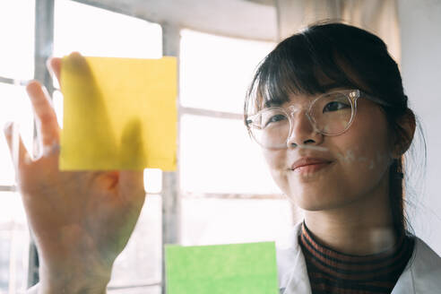 Junge Wissenschaftlerin klebt Haftnotiz auf transparentes Glas im Labor - ASGF01890