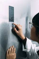 Junge Wissenschaftlerin, die bei der Arbeit im Labor auf ein Bedienfeld zeigt - ASGF01896