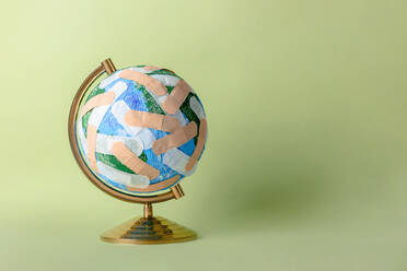 Runder Globus des Planeten Erde, beklebt mit zahlreichen medizinischen Pflastern auf hellgrünem Hintergrund - ADSF32728