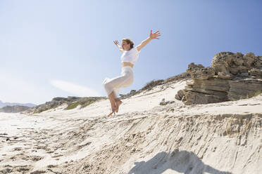 Ein junges Mädchen springt von einer Sanddüne in den weichen Sand darunter. - MINF16476