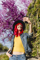 Frau mit Hand in der Tasche, die ein Selfie mit ihrem Smartphone an einem sonnigen Tag macht - MRRF01746