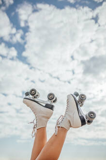 Raised legs of cop anonymous sportive female in roller skates against blue sky with clouds on sunny day on street - ADSF32741