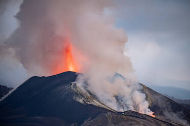 Atemberaubende Luftaufnahme einer Berglandschaft mit dem ausbrechenden Vulkan Cumbre Vieja, der Magma ausstößt, bedeckt von dichtem Rauch auf der Insel La Palma - ADSF32744
