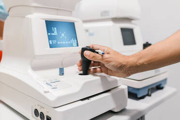 Crop anonymous male doctor ophthalmologist conducting autorefractometry of ocular pressure of female patient on modern equipment of pneumotonometer in ophthalmological clinic - ADSF32745