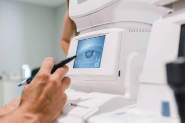 Anonymer männlicher Augenarzt, der die Autorefraktometrie des Augendrucks einer Patientin mit einem modernen Pneumotonometer in einer Augenklinik durchführt - ADSF32746