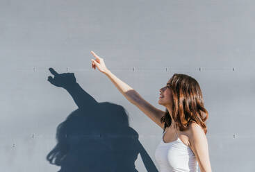 Side view of ethnic lady in white top pointing index finger up near gray wall - ADSF32764