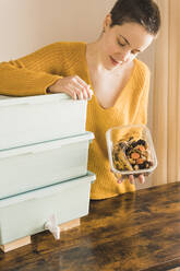 Woman holding organic waste box and vermicompost container at table - MGRF00591