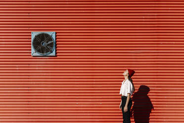 Young woman standing with eyes closed at red corrugated wall - EGAF02466