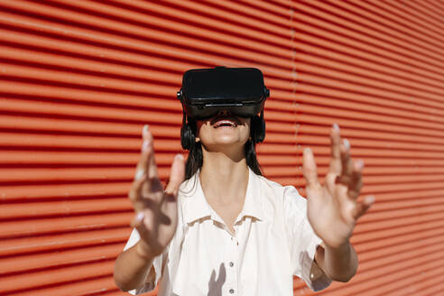Lächelnde junge Frau mit Virtual-Reality-Headset an einem sonnigen Tag - EGAF02470