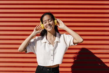 Woman listening music through headphones in front of wall - EGAF02474