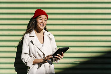 Lächelnde junge Frau mit Tablet-PC vor einer Wand - EGAF02494