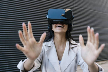 Smiling woman using virtual reality headset in front of wall - EGAF02508