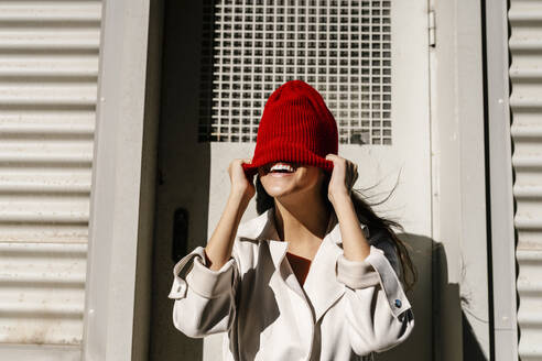 Woman hiding face with knit hat in front of door - EGAF02511