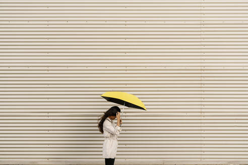 Frau hält Regenschirm an weißer Wellblechwand - EGAF02517