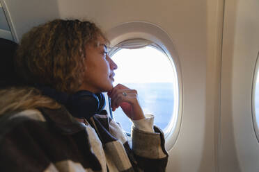 Junge Frau mit Hand am Kinn schaut aus dem Flugzeugfenster - MRAF00799