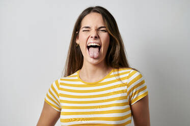 Fröhliche Frau streckt die Zunge heraus und zwinkert auf grauem Hintergrund - KIJF04338