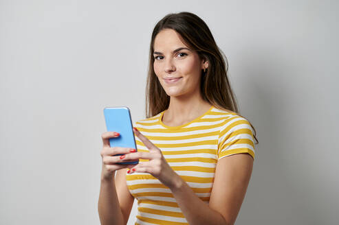 Junge Frau hält Handy vor grauem Hintergrund - KIJF04339