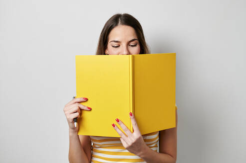 Junge Frau liest gelbes Buch auf grauem Hintergrund - KIJF04343