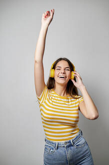 Junge Frau mit erhobener Hand tanzt vor grauem Hintergrund - KIJF04350