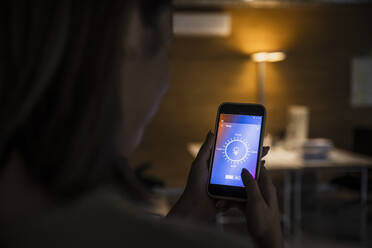 Woman using smart phone with light bulb icon screen at home - UUF25287