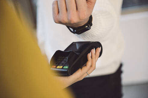 Man paying through smart watch to waitress holding credit card reader in cafe - UUF25290