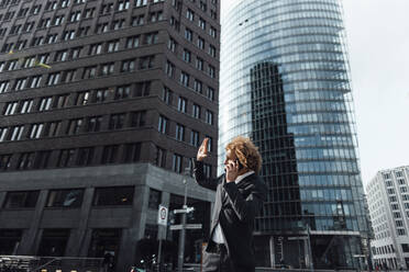 Businessman shielding face and talking on mobile phone in city - GUSF06684