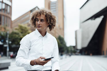 Businessman holding mobile phone in city - GUSF06693