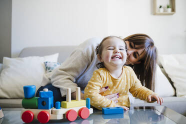 Mother embracing cheerful daughter with toys at table - EBBF05081