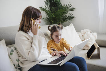 Mutter mit Laptop, die zu Hause mit ihrer Tochter über ein Mobiltelefon spricht - EBBF05101