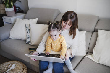 Mutter benutzt Laptop mit Tochter auf Sofa - EBBF05102