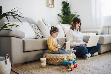 Frau und kleines Mädchen benutzen Laptop und Tablet-PC im Wohnzimmer - EBBF05105