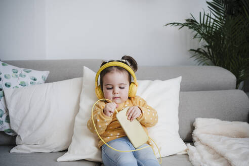 Baby-Mädchen steckt Kopfhörer in Handy auf Sofa - EBBF05107