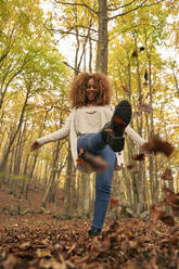 Happy woman kicking leaves in autumn forest - VEGF05231