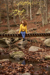 Frau sitzt auf einer Holzbrücke im Herbstwald - VEGF05232