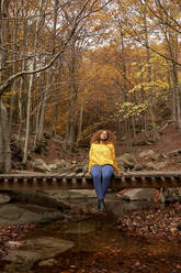 Frau entspannt auf Holzbrücke im Herbstwald - VEGF05237