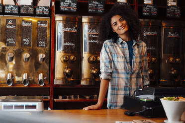 Smiling owner standing at cash register in coffee roastery - KNSF09186
