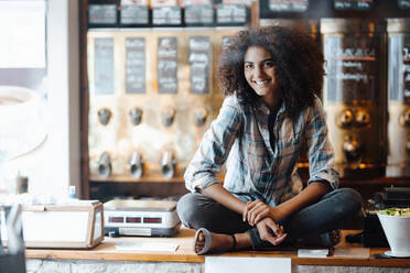 Businesswoman sitting cross-legged on counter at coffee roastery - KNSF09212